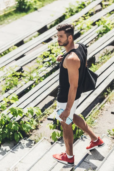 Deportista sosteniendo botella de agua y bolsa para equipos deportivos en escaleras en el patio de recreo deportivo - foto de stock