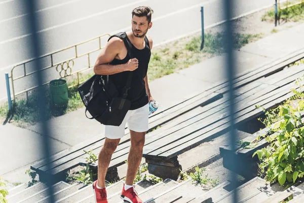 Junger Sportler hält Wasserflasche und Tasche für Sportgeräte auf Treppe am Sportplatz — Stockfoto