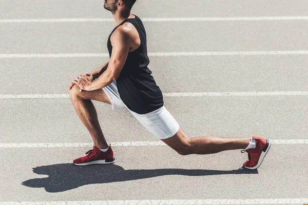 Immagine ritagliata di jogger maschile che si estende sulla pista da corsa al parco giochi sportivo — Foto stock