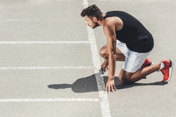 Visão lateral do jovem atleta do sexo masculino em baixo início na pista de corrida — Fotografia de Stock