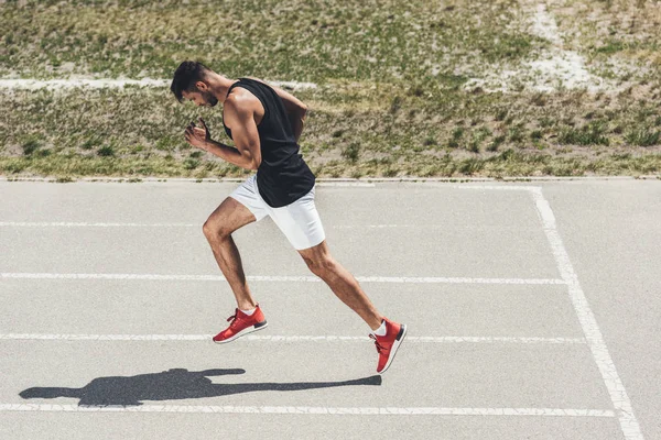 Vista lateral del velocista masculino corriendo en pista atlética en el patio de recreo deportivo - foto de stock