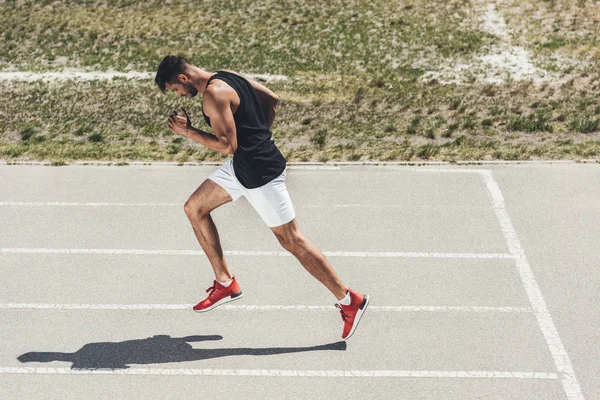 Side view of male sprinter running on athletic track at sport playground — Stock Photo