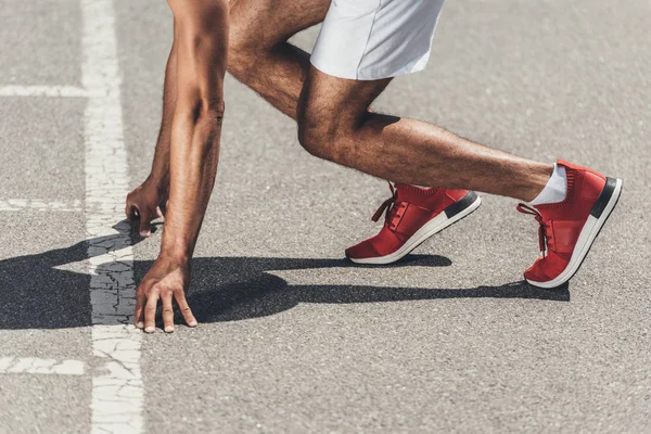 Imagen recortada del velocista masculino en posición inicial en la pista de rodadura - foto de stock