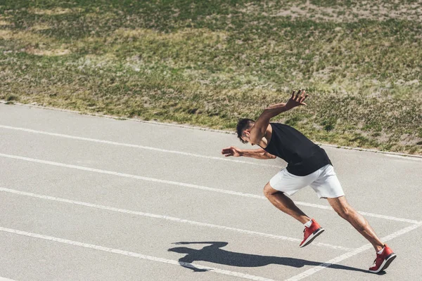 Joven sprinter macho despegando de la posición inicial en pista de atletismo - foto de stock