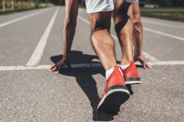Ausschnittbild eines männlichen Sprinters in Startposition auf Laufstrecke — Stockfoto
