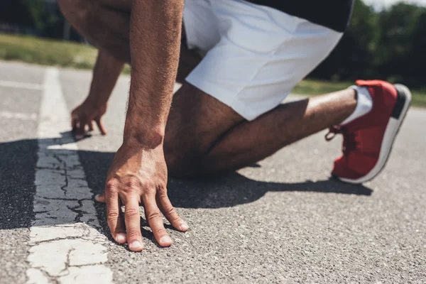 Cropped image of male sprinter in starting position on running track — Stock Photo