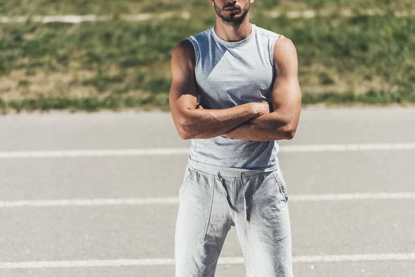 Cropped shot of sporty young man with crossed arms on running track — Stock Photo