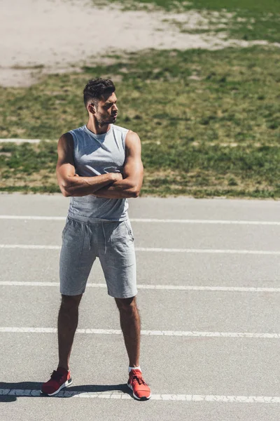 Jeune homme sérieux avec les bras croisés sur la piste de course — Photo de stock