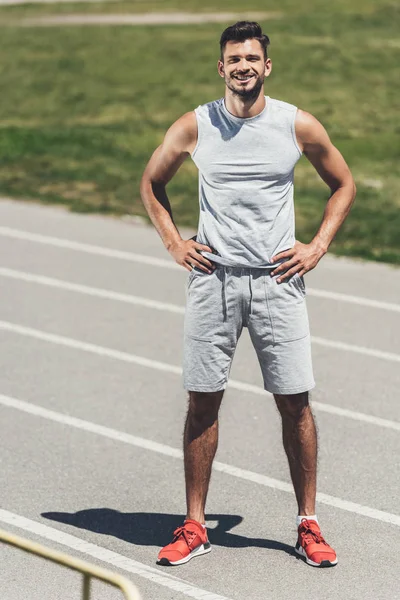 Feliz joven de pie en pista de atletismo con los brazos akimbo - foto de stock