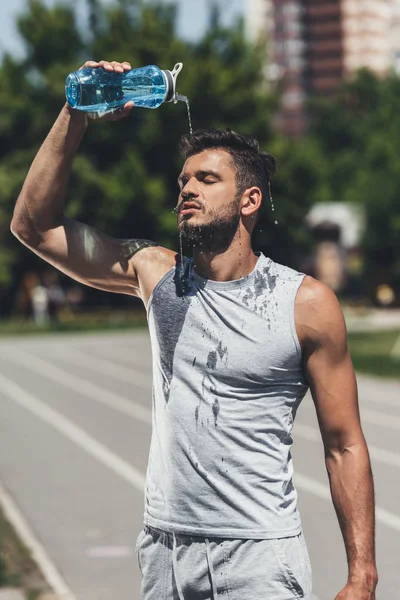 Jeune homme athlétique verser de l'eau sur lui-même après l'entraînement — Photo de stock