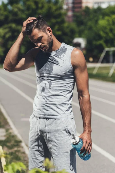 Schöner junger Mann im nassen Hemd mit Fitnessflasche auf Laufstrecke — Stockfoto