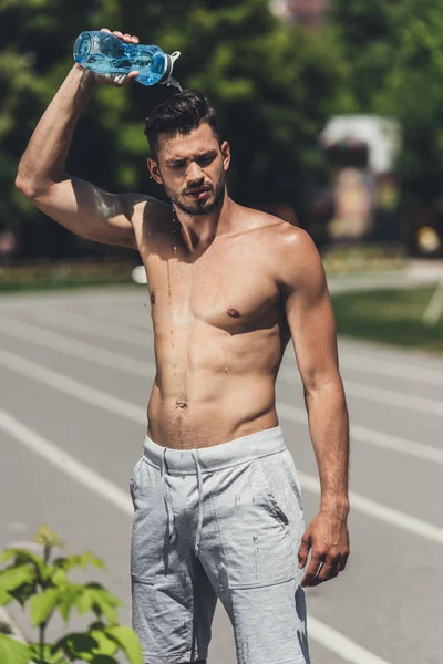 Guapo sin camisa joven vertiendo agua sobre sí mismo después de entrenar - foto de stock