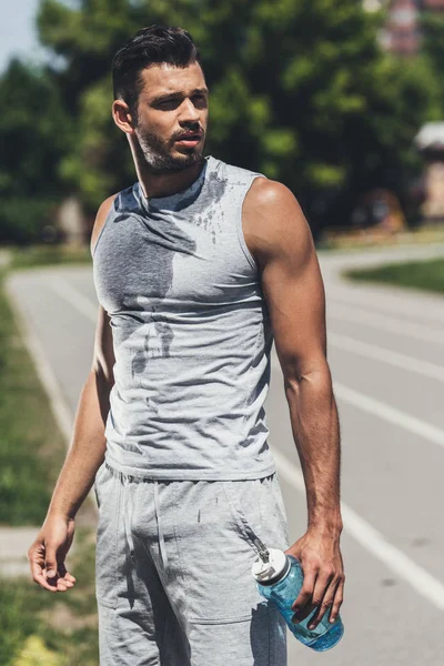 Bello bagnato giovane uomo con bottiglia di fitness su pista da corsa — Foto stock