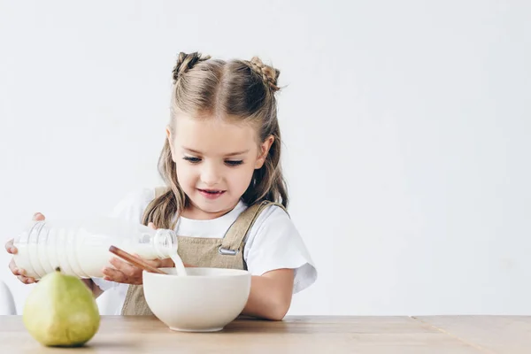 Little schoolgirl pouring milk into bowl with breakfast isolated on white — Stock Photo