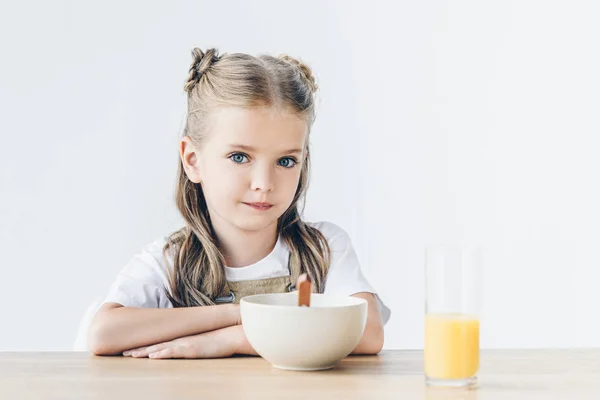 Confident little schoolgirl sitting at table with breakfast isolated on white — Stock Photo