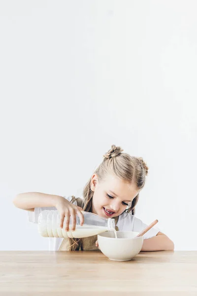 Sorridente scolaretta versando latte nei cereali per colazione isolata su bianco — Foto stock