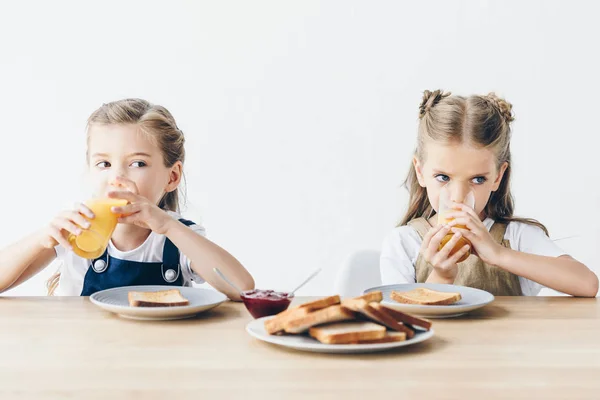 Schöne kleine Schwestern, die Toasts mit Marmelade essen und Orangensaft zum Frühstück trinken, isoliert auf weiß — Stockfoto