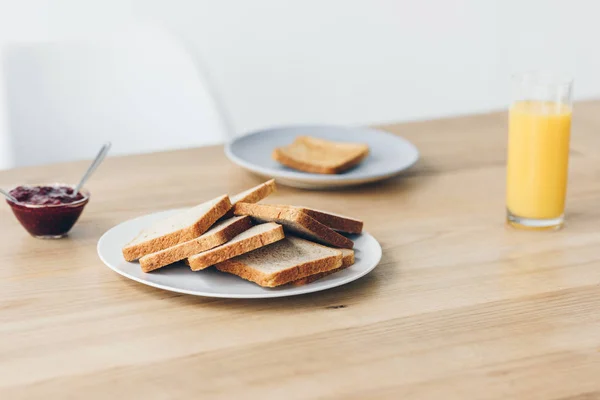 Nahaufnahme eines Tellers mit Toasts auf dem Tisch mit einer Schüssel Marmelade und Orangensaft zum Frühstück — Stockfoto