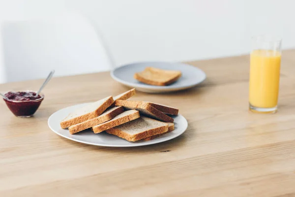 Tiro de close-up de prato com torradas na mesa com tigela de geléia e suco de laranja para o café da manhã — Fotografia de Stock