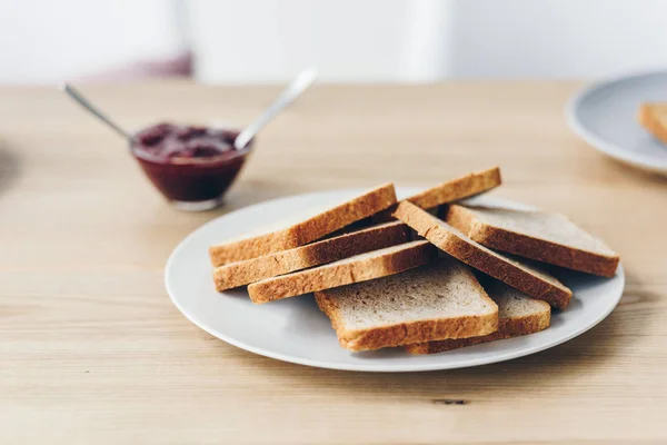 Plan rapproché de la plaque avec des toasts sur la table avec bol de confiture pour le petit déjeuner — Photo de stock