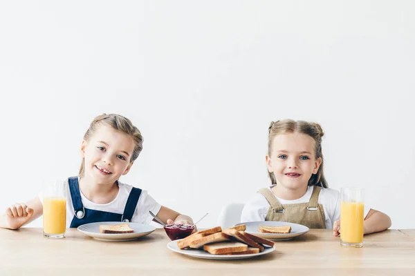 Sorelline che mangiano pane tostato con marmellata a colazione e guardando la telecamera isolata su bianco — Foto stock