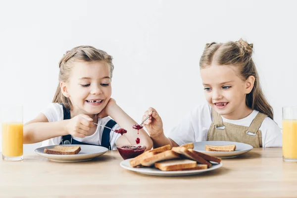 Adorables petites sœurs manger des toasts avec confiture pour le petit déjeuner isolé sur blanc — Photo de stock