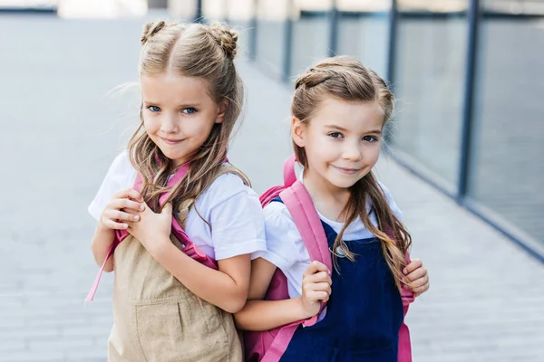 Smiling little schoolgirls with pink backpacks on street looking at camera — Stock Photo