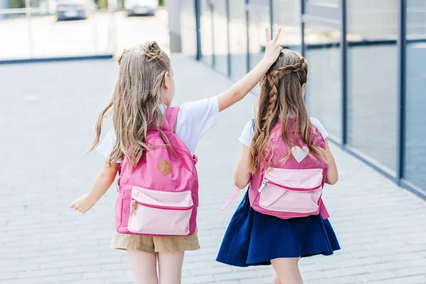 Rückansicht einer kleinen Schülerin, die ihrem Klassenkameraden auf der Straße Hupen macht — Stockfoto