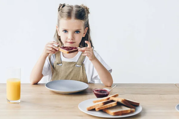Beautiful little schoolgirl eating toast with jam isolated on white — Stock Photo