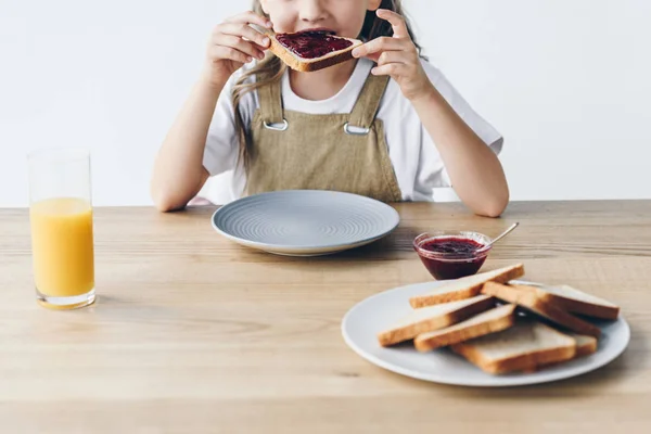 Tiro recortado de niño pequeño comiendo tostadas con mermelada aislada en blanco - foto de stock