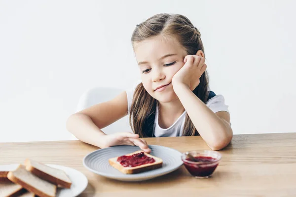 Bored little schoolgirl with toasts and jam for breakfast isolated on white — Stock Photo