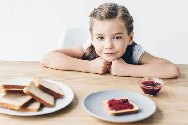 Adorable little schoolgirl with toasts and jam for breakfast looking at camera isolated on white — Stock Photo