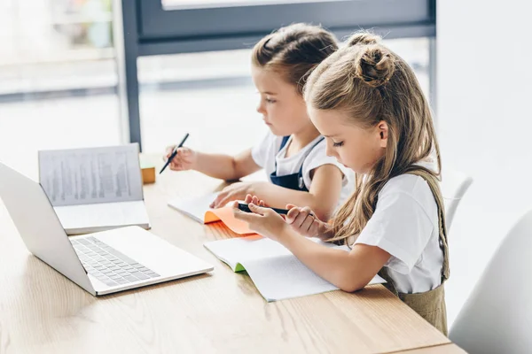 Kleine Schulmädchen mit Laptop und Notizbuch zum Lernen isoliert auf weiß — Stockfoto