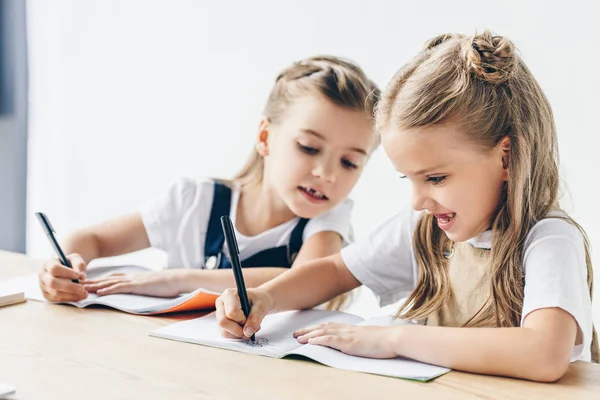 Pequeña colegiala haciendo trampa y copiando el trabajo de su compañero de clase aislado en blanco - foto de stock