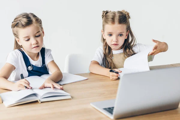 Piccole studentesse che studiano con computer portatile sulla scrivania isolata su bianco — Foto stock