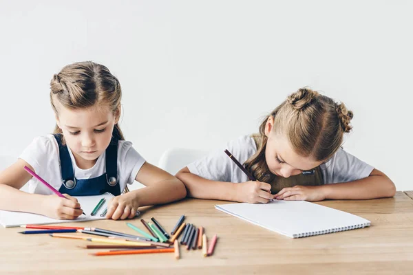 Adorable little schoolgirls drawing with colorful pencils in albums together isolated on white — Stock Photo