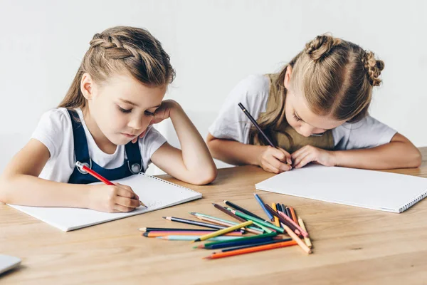 Concentrated little schoolgirls drawing with colorful pencils in albums together isolated on white — Stock Photo