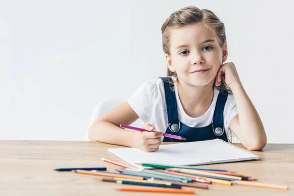 Pequena colegial feliz desenho com lápis de cor e olhando para a câmera isolada no branco — Fotografia de Stock