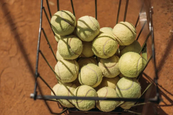 Panier de balles de tennis debout sur la surface du court orange — Photo de stock