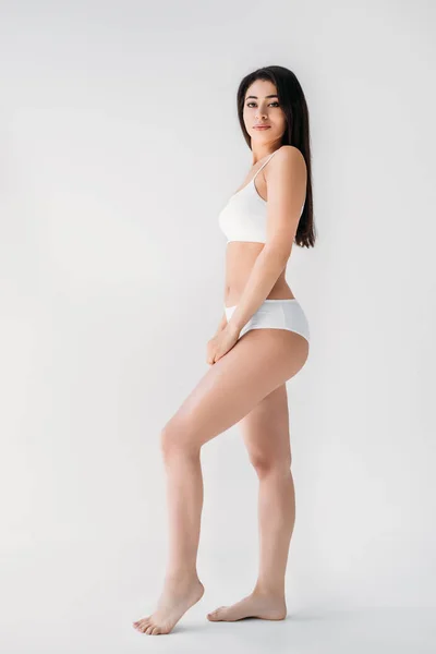 Atractiva mujer de raza mixta en lencería blanca posando aislada sobre fondo gris - foto de stock