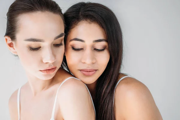 Retrato de dos atractivas mujeres multiculturales posando aisladas sobre fondo gris - foto de stock