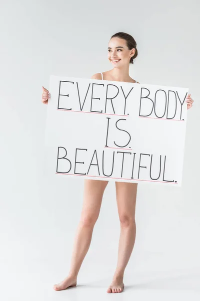 Sorrindo mulher caucasiana segurando banner com letras cada corpo é bonito isolado no fundo cinza — Fotografia de Stock