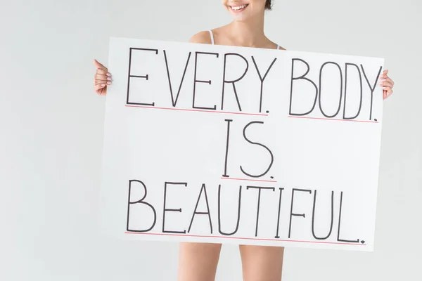 Image recadrée d'une femme souriante tenant une bannière avec lettrage chaque corps est beau isolé sur fond gris — Photo de stock
