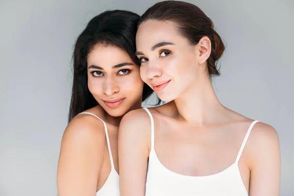 Sonrientes mujeres multiculturales mirando a la cámara aislada sobre fondo gris - foto de stock