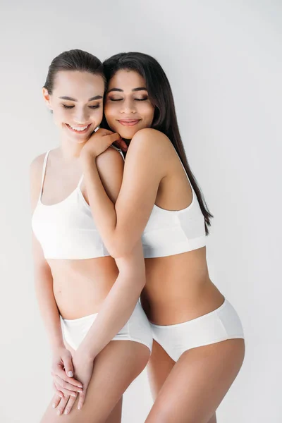 Lächelnde multikulturelle Frauen, die sich isoliert auf grauem Hintergrund umarmen — Stockfoto