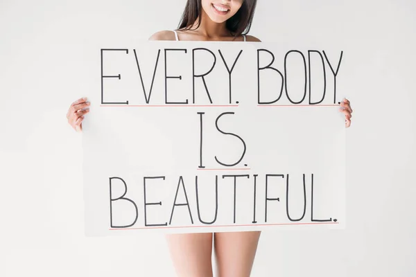 Imagen recortada de mujer sonriente sosteniendo pancarta con letras cada cuerpo es hermoso aislado sobre fondo gris - foto de stock