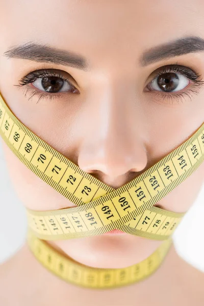 Portrait of attractive young woman with closed mouth by measurement tape isolated on gray background — Stock Photo
