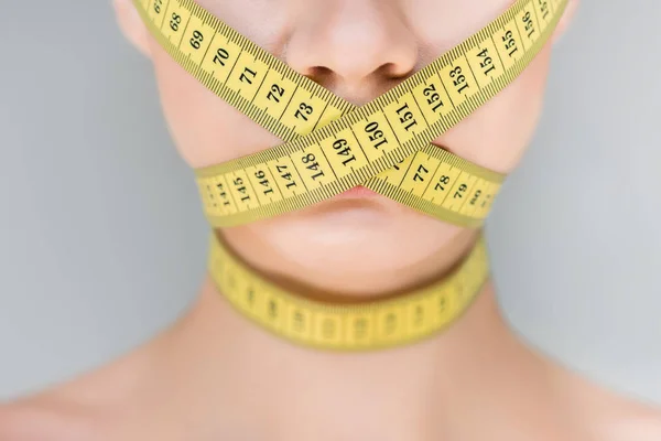 Обрезанное изображение женщины с закрытым ртом с помощью измерительной ленты, изолированной на сером фоне — стоковое фото