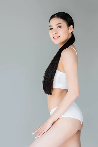 Atractiva mujer asiática en lencería blanca posando sobre fondo gris - foto de stock
