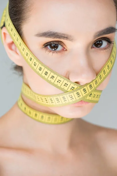 Retrato de mujer joven atractiva con la boca cerrada por cinta métrica aislada sobre fondo gris - foto de stock